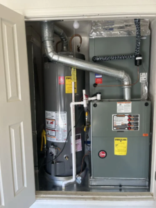 A gas furnace installed in a narrow storage closet, with its front panel removed to show internal components. A yellow EnergyGuide label is visible on the sid